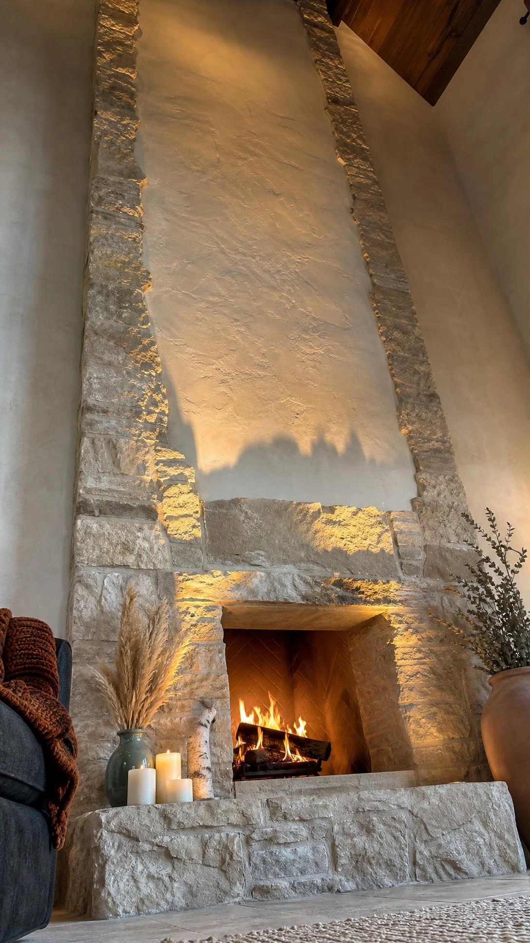 Floor-to-ceiling stacked limestone fireplace wall photographed from ground level, showcasing dramatic vertical height and natural ivory fossil-textured stone in a modern interior