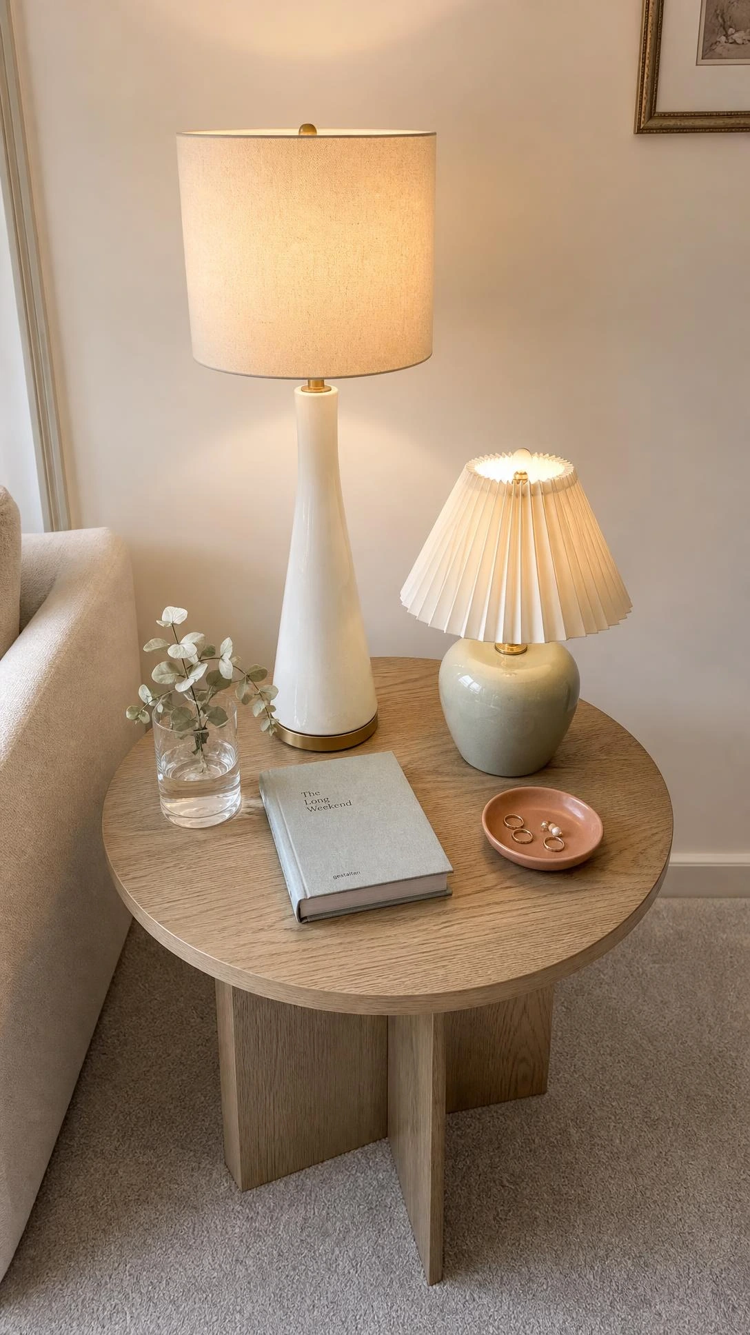 Two mismatched table lamps at different heights on a sage green side table — a tall slim white ceramic lamp paired with a shorter chunky sage base lamp, creating budget-friendly layered lighting