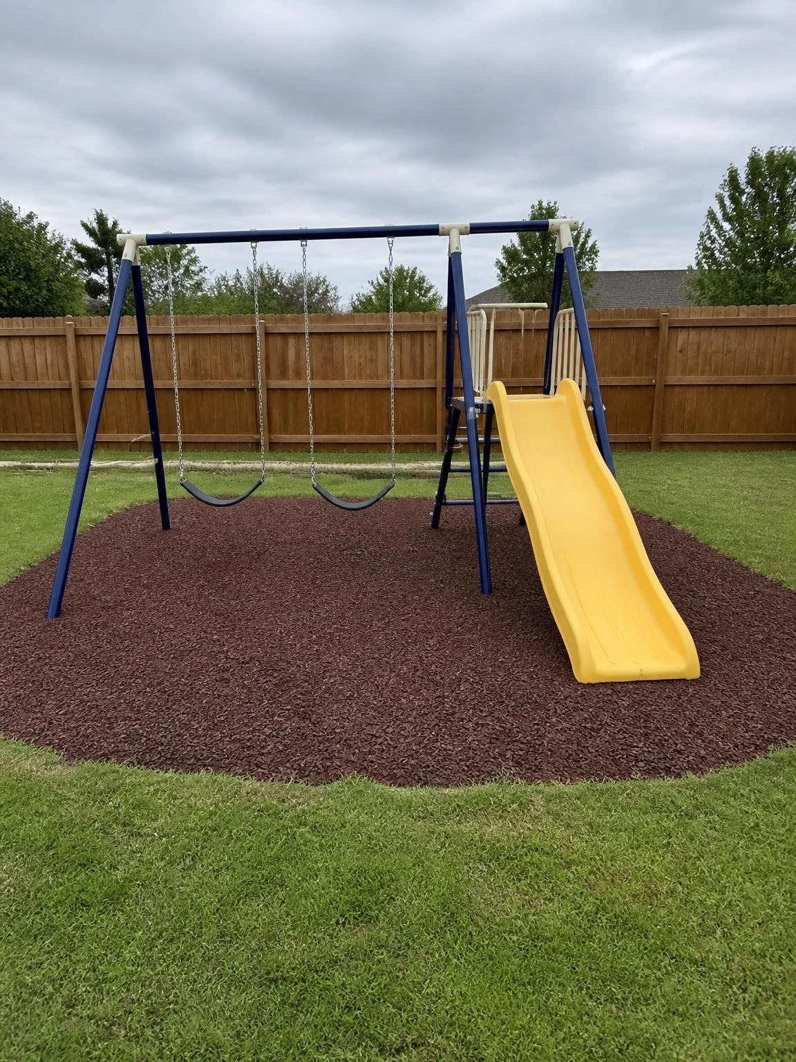 Navy powder-coated steel A-frame swing set with two belt swings and yellow plastic slide on rubber mulch safety surfacing in compact suburban backyard