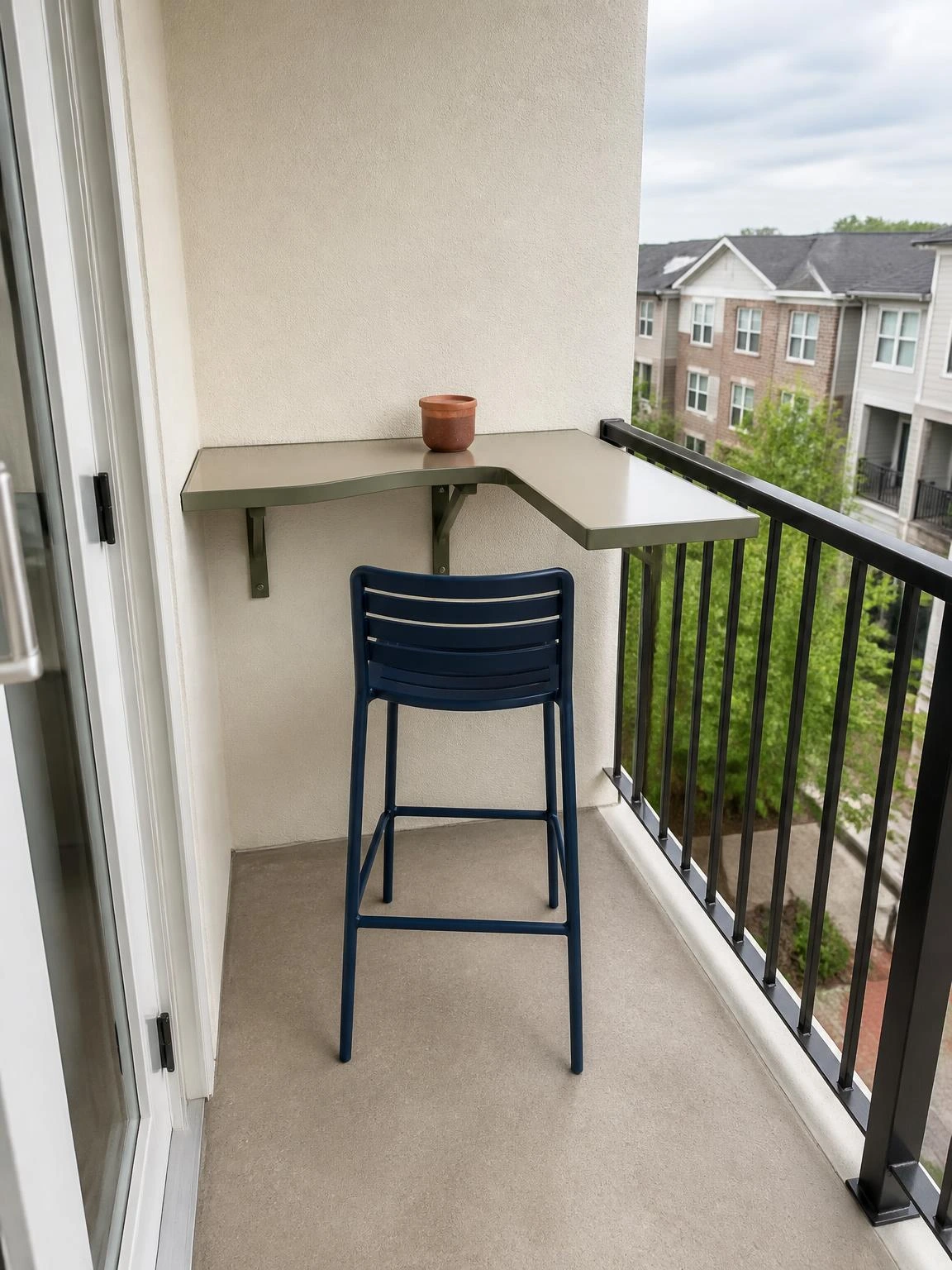 Small balcony corner bistro bar with an L-shaped wall-mounted counter, navy stool, and terracotta cup beside the door