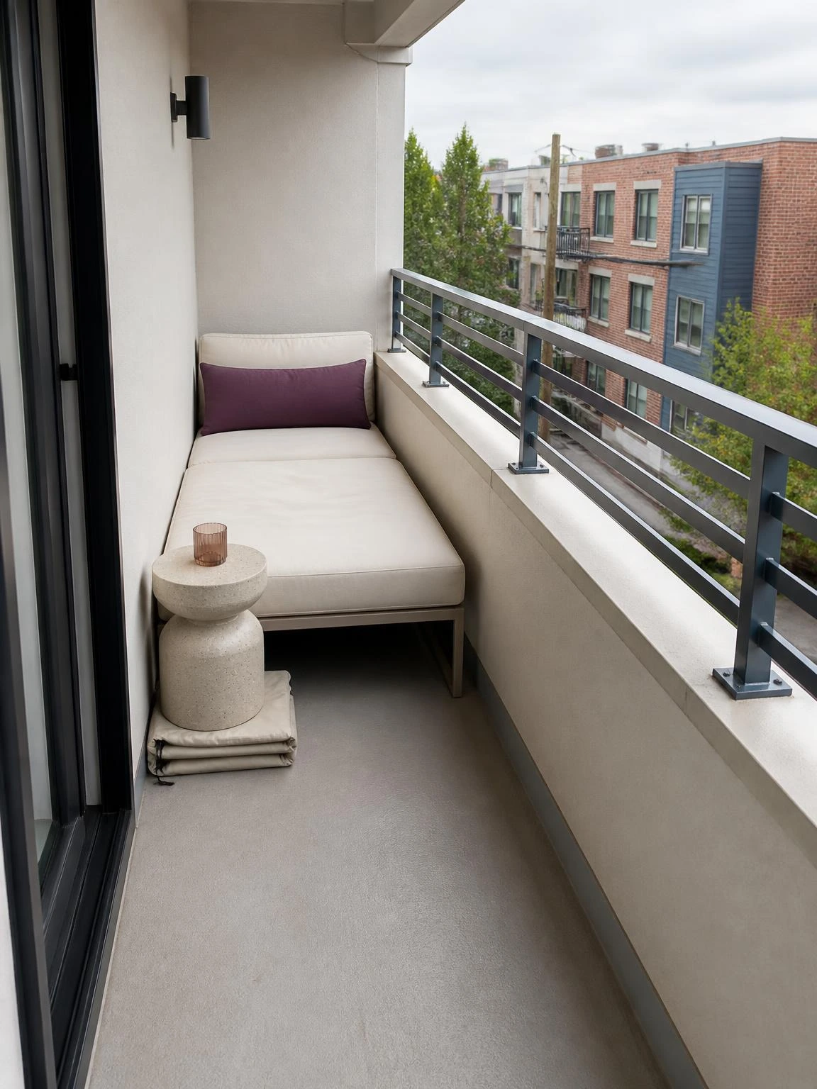 Balcony corner daybed with ivory cushion, plum lumbar pillow, stone table, and open passage beside the visible railing