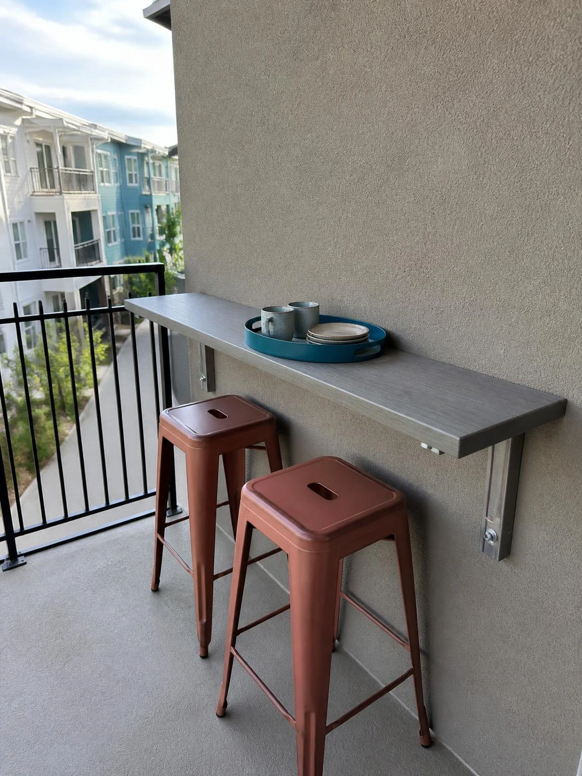 Slim wall-mounted balcony outdoor bar shelf with rust stools and a muted blue serving tray for compact entertaining