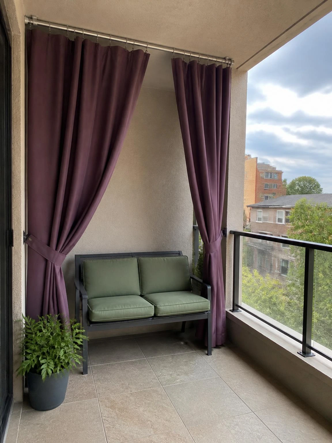 Muted plum outdoor curtains screen a two-seat balcony bench while preserving daylight, airflow, and an open residential view.