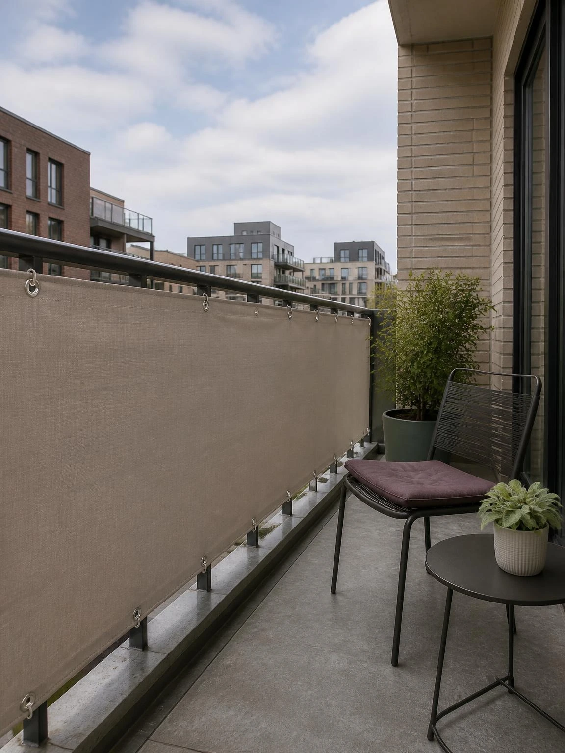 Stone outdoor fabric screen secures a city balcony railing, creating practical balcony privacy beside a charcoal chair and green plant.