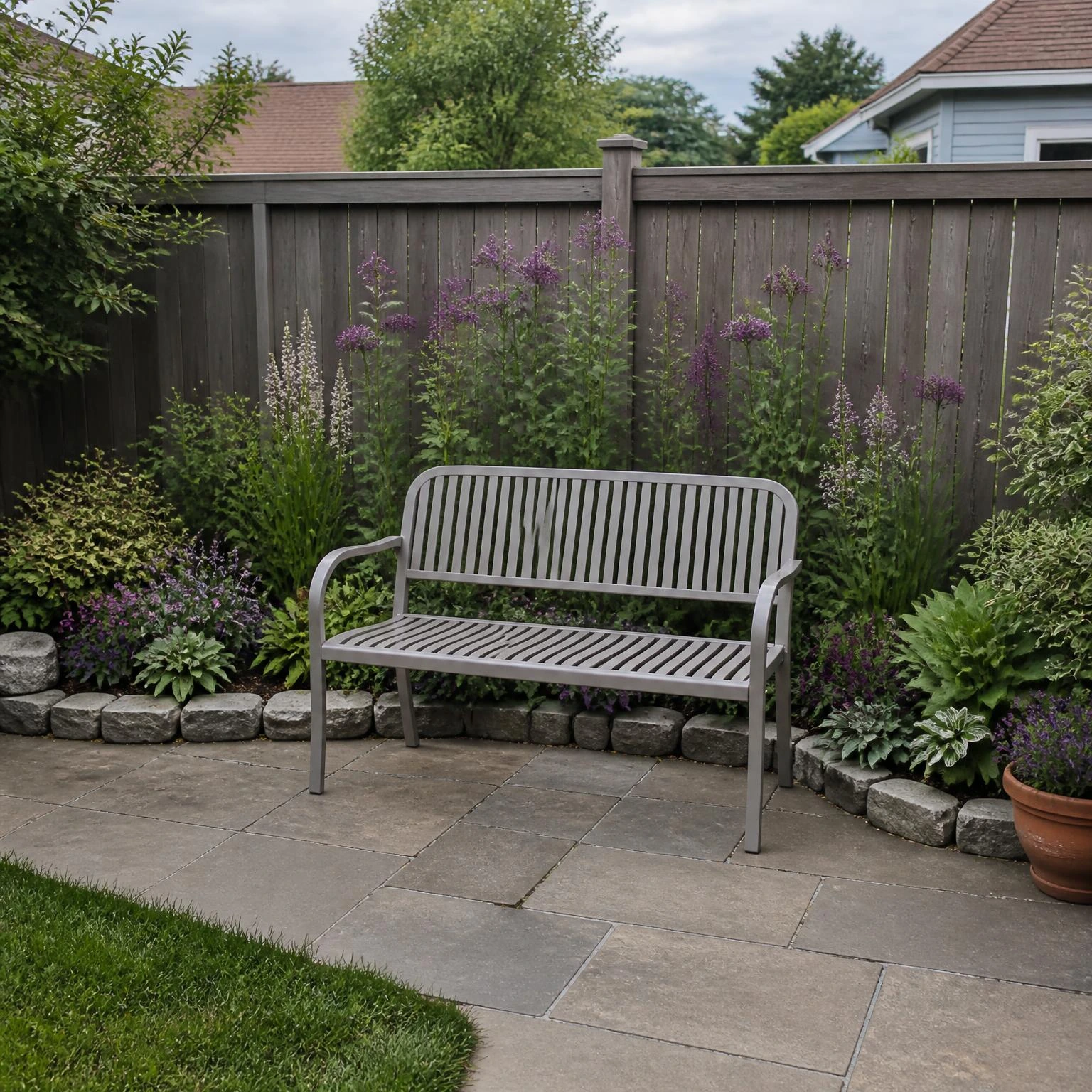 Small backyard flower garden ideas featuring a warm-gray bench beside a narrow, stone-edged flower bed and rear fence.