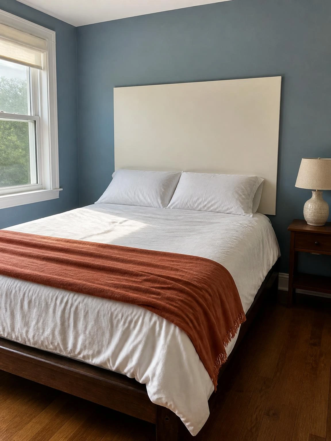 DIY plywood panel headboard painted warm white mounted on dusty blue bedroom wall above a low dark-stained bed frame with white pillows