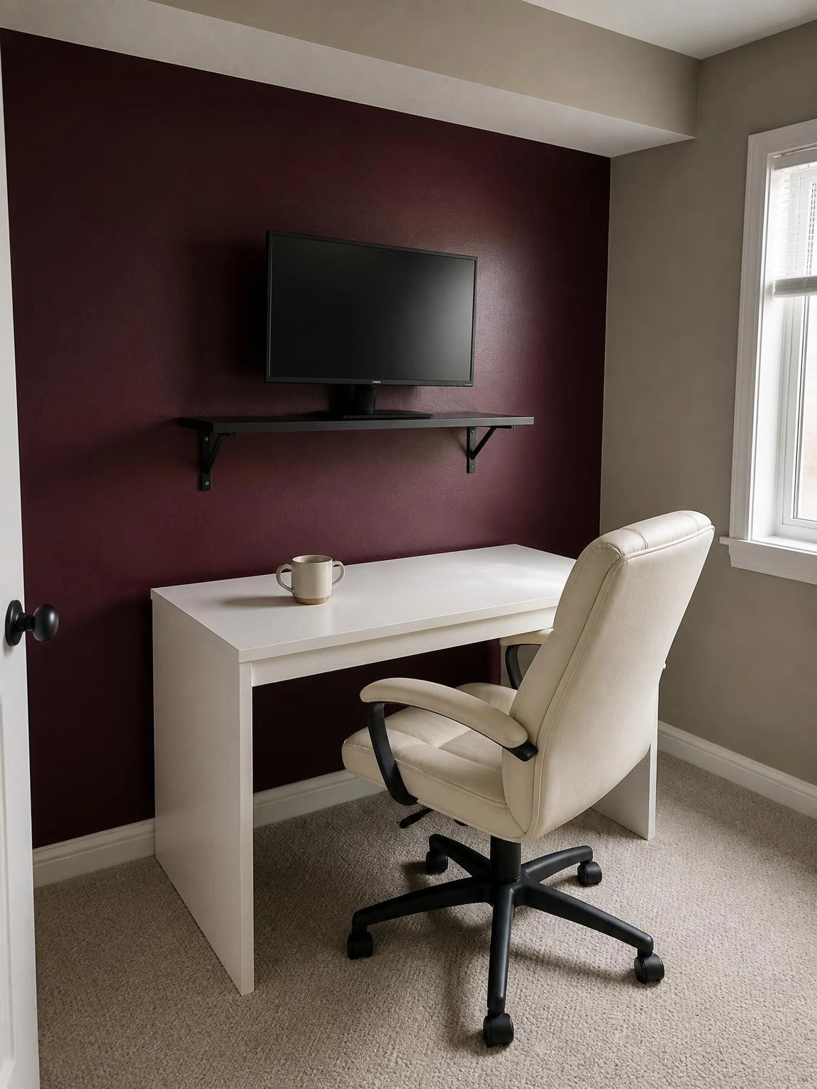 Compact home office with a deep burgundy accent wall behind a white laminate desk and ivory chair, showing a bold summer color refresh in a small workspace