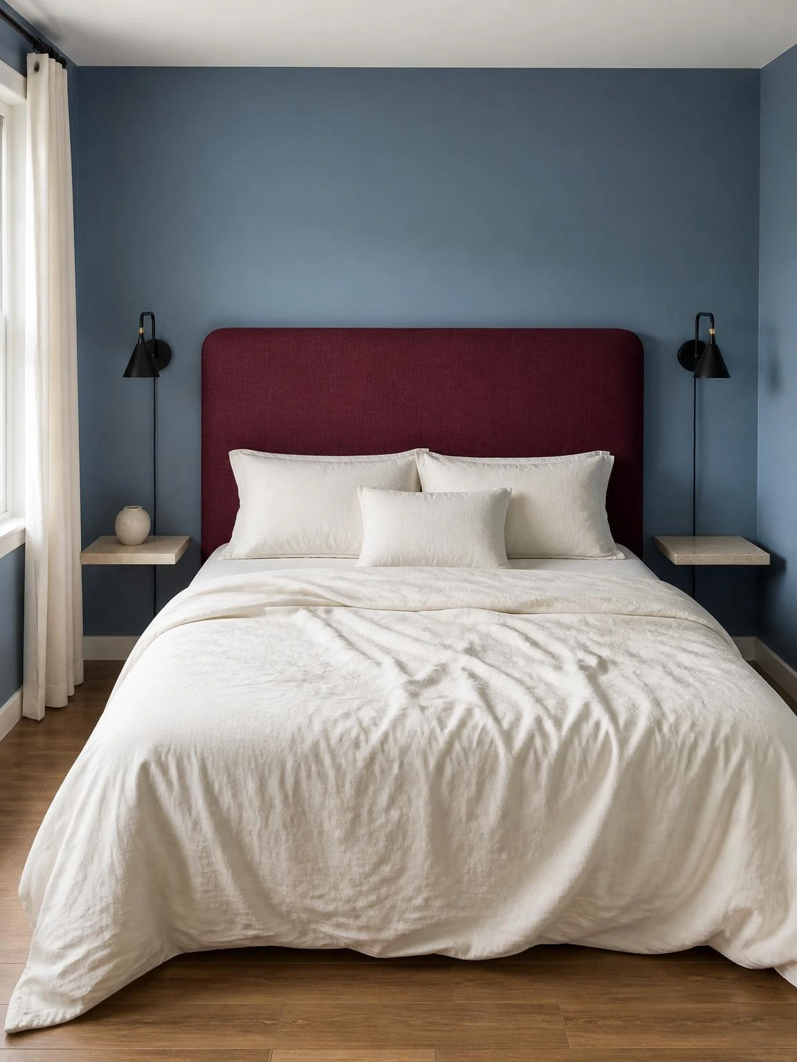 Burgundy linen headboard anchors a compact bedroom with ivory bedding, muted blue walls, and black sconces for Halloween aesthetic bedroom decor
