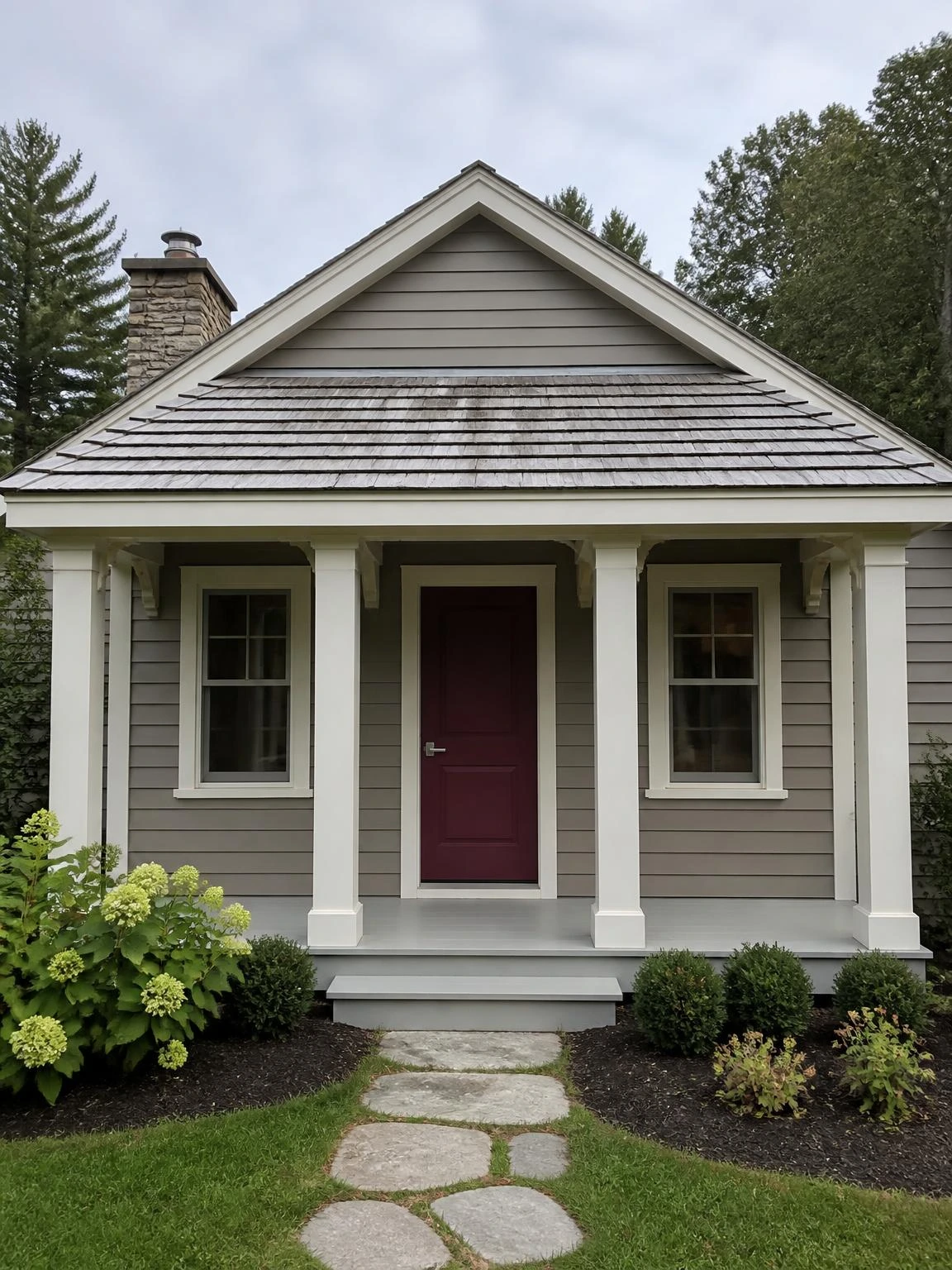 Cedar shake porch roof on a cottage-style home, showing weathered silver-gray shakes with natural tone variation above ivory trim and a burgundy front door