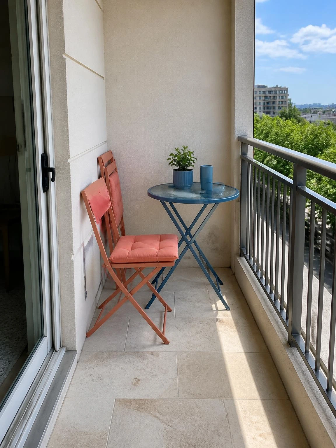 Compact bistro balcony with coral folding chairs, a round café table, and a clear path to the door