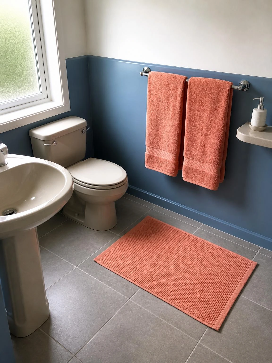 Soft coral cotton towels hung on a chrome rail with a matching bath mat on grey tiles — a simple summer bathroom refresh