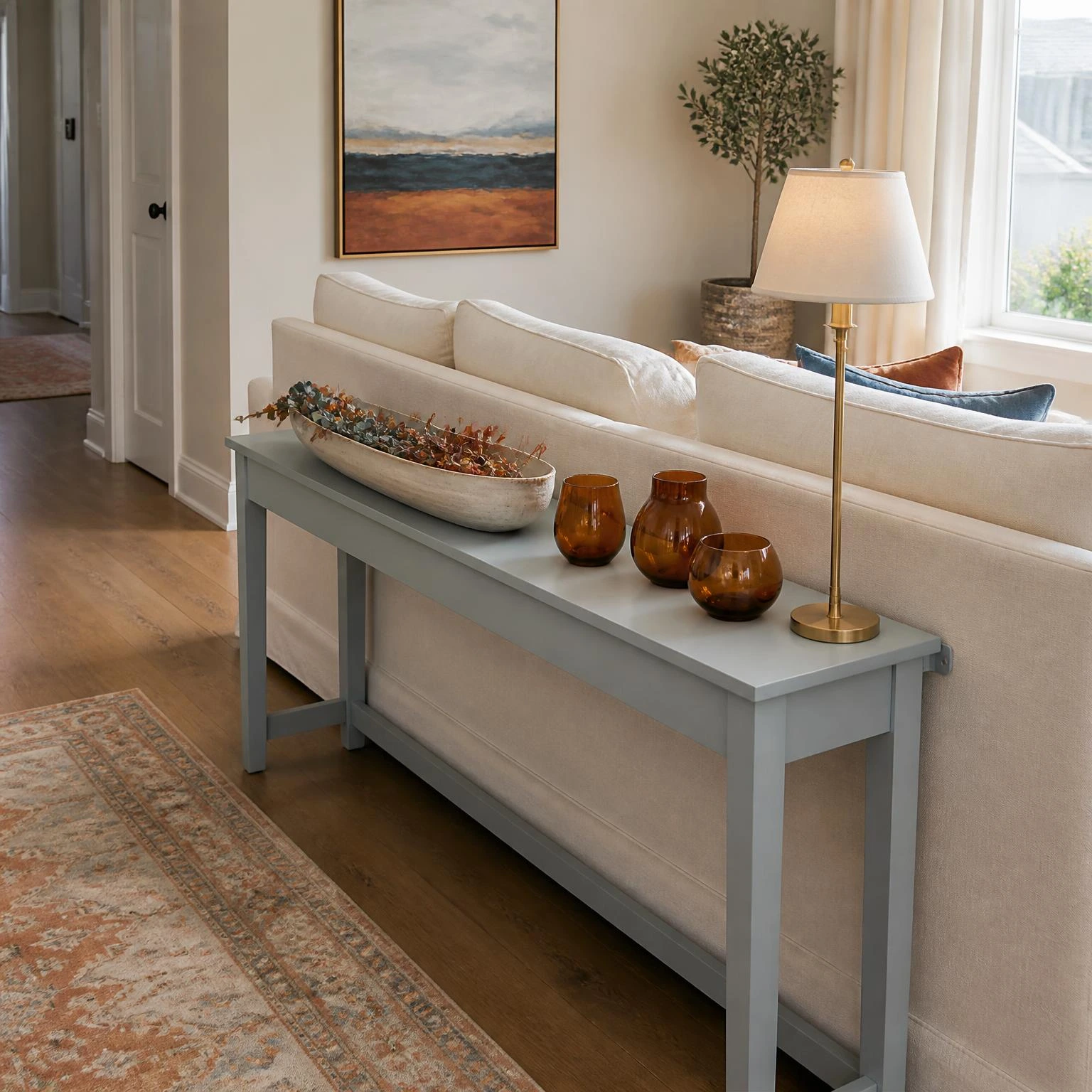 Fall console table display behind a warm-white sofa, styled with stoneware, brass, and amber vessels in a usable living room