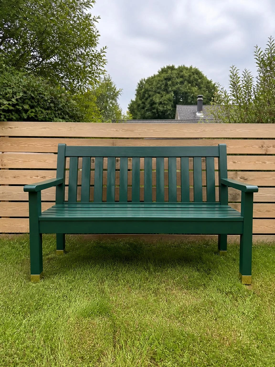 Two-seat timber garden bench repainted in deep forest green against warm neutral fence boards, showing how a simple colour change transforms tired outdoor furniture