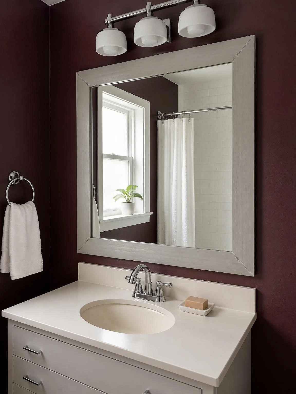 DIY trim molding frame in warm gray surrounds a builder-grade bathroom mirror on a deep burgundy wall, showing clean mitered corners and a polished finished look