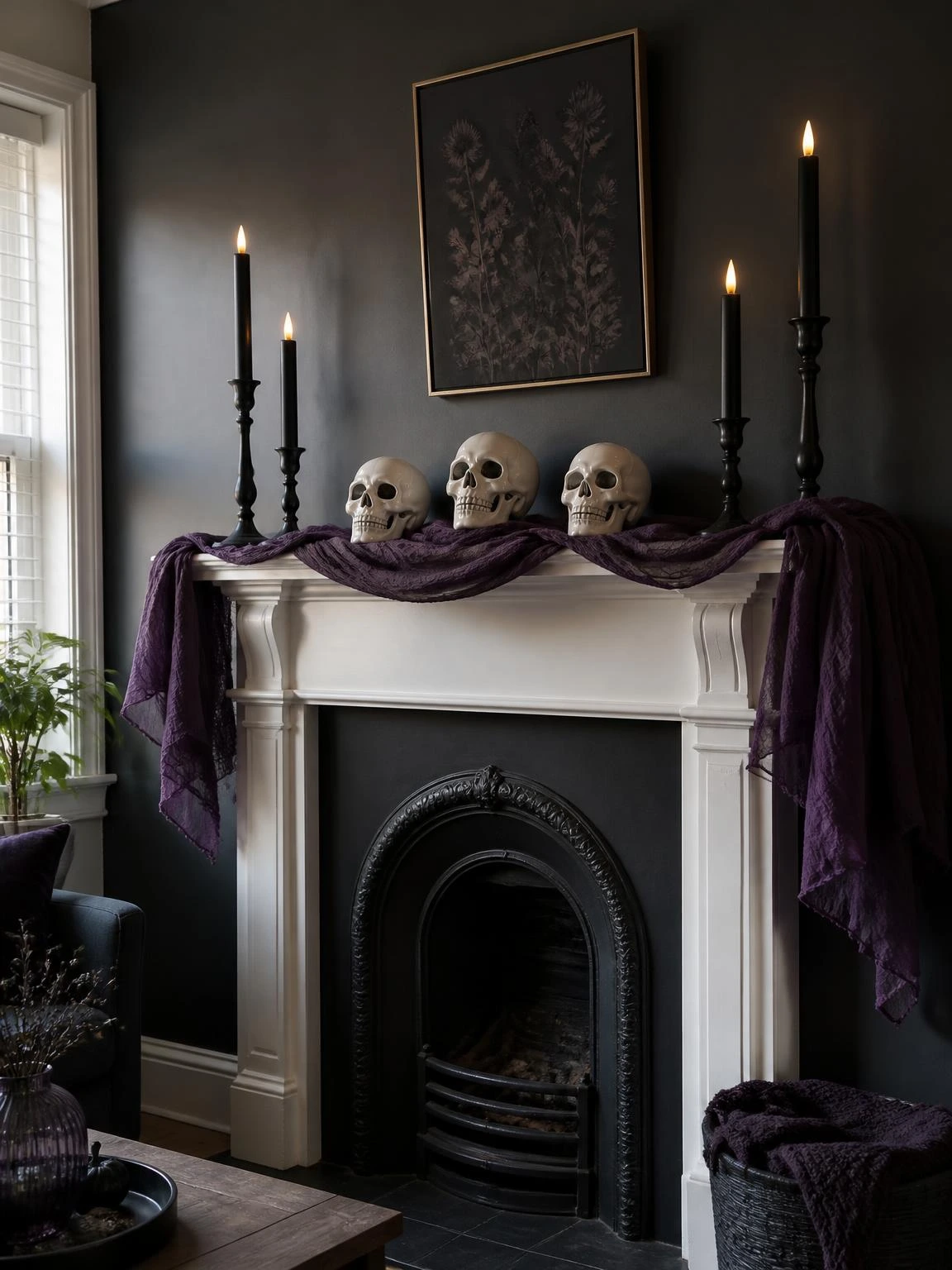 Gothic Halloween fireplace mantel with black iron taper holders, bone-white ceramic skulls, and purple draped fabric against a charcoal wall