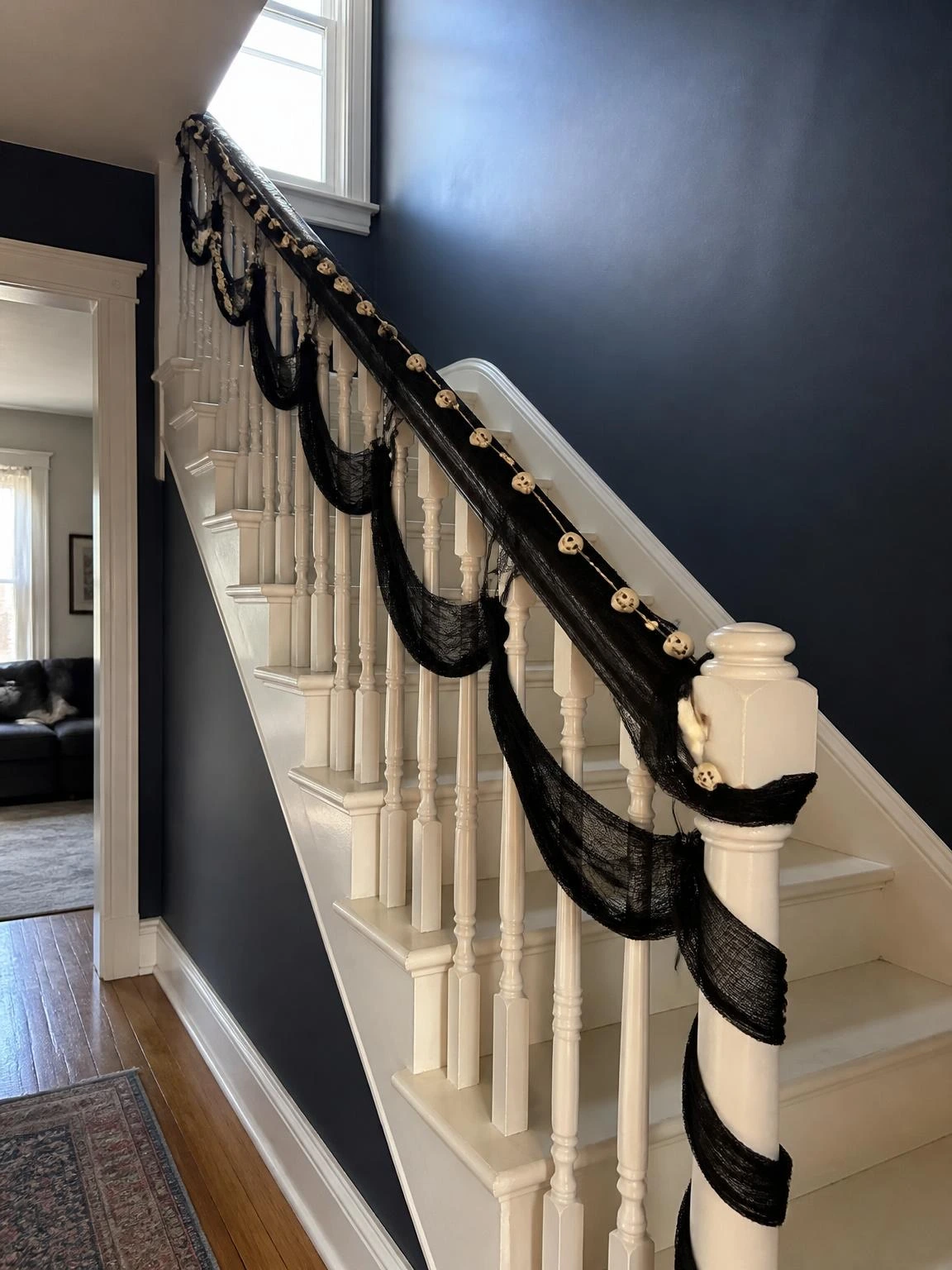 Black gauze fabric loosely wound around white balusters with an ivory skull bead garland following the handrail line — gothic halloween decorations that feel haunted-house rather than party-store