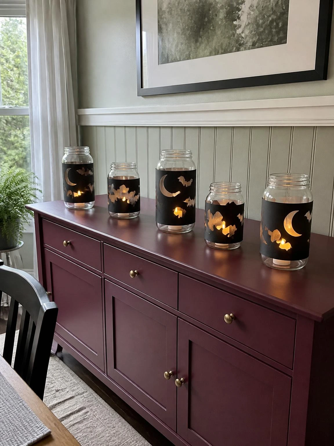 Halloween crafts DIY projects featuring clear jars with black moon and bat wraps, glowing on a dining-room sideboard