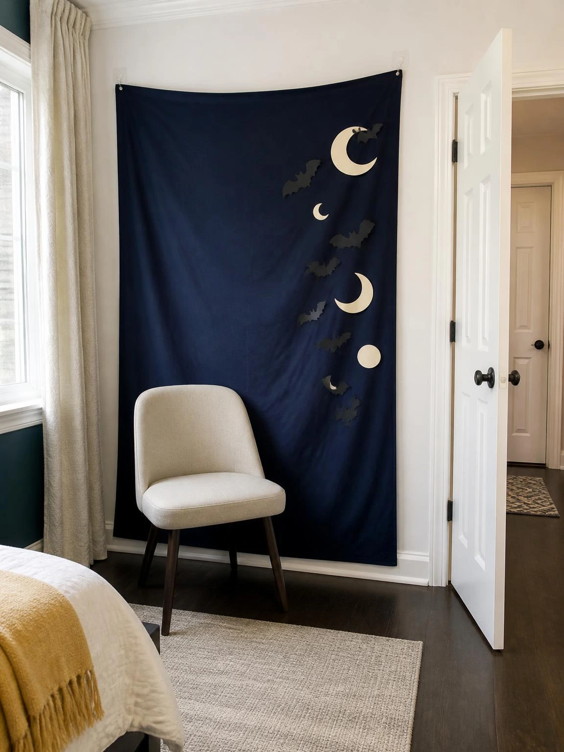 Navy fabric, paper moons, and black bats create a DIY Halloween bedroom decor photo backdrop beside a functional chair.