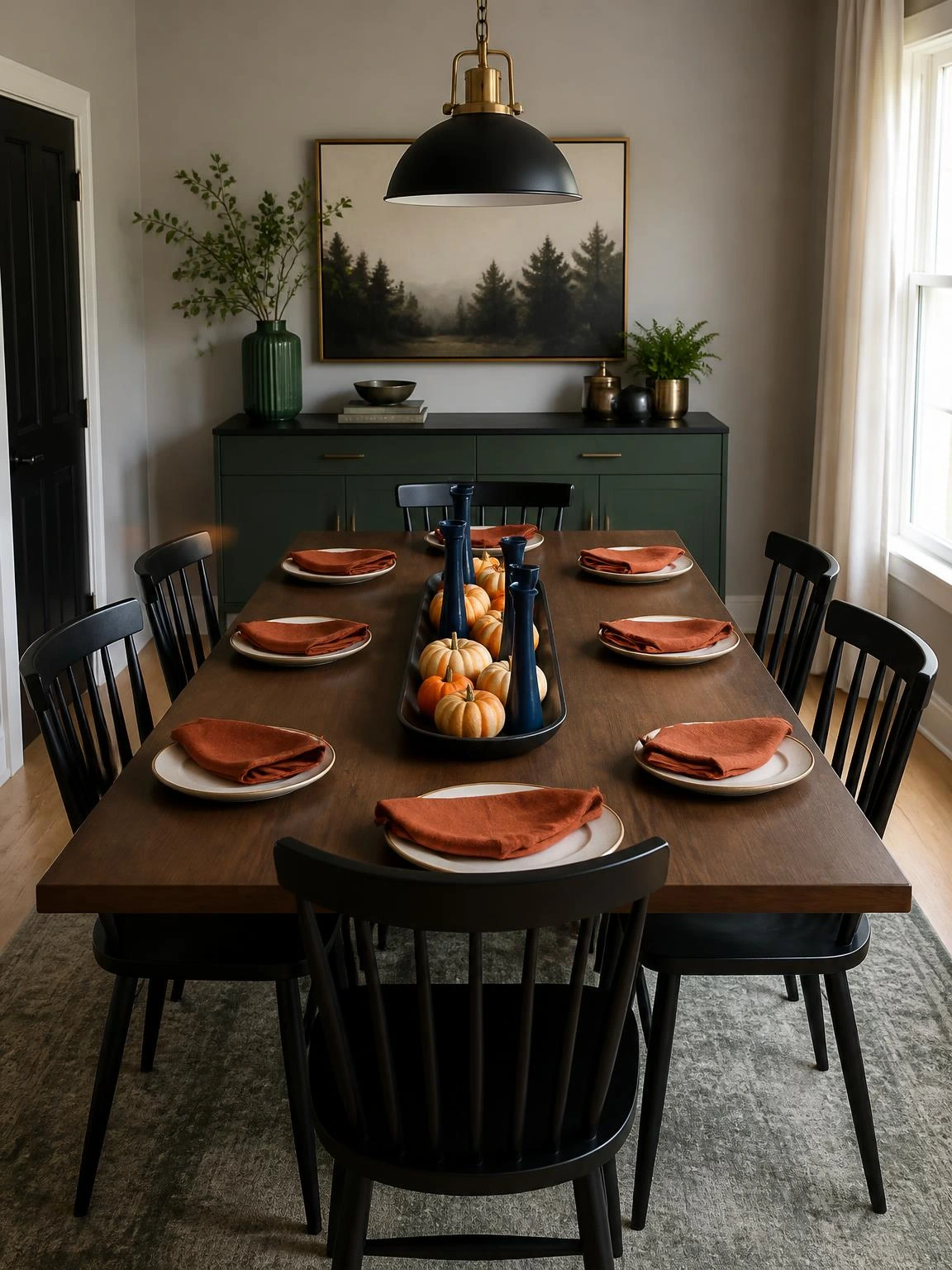 A low black tray of miniature pumpkins and navy candleholders anchors a practical Halloween dining centerpiece with rust napkins.