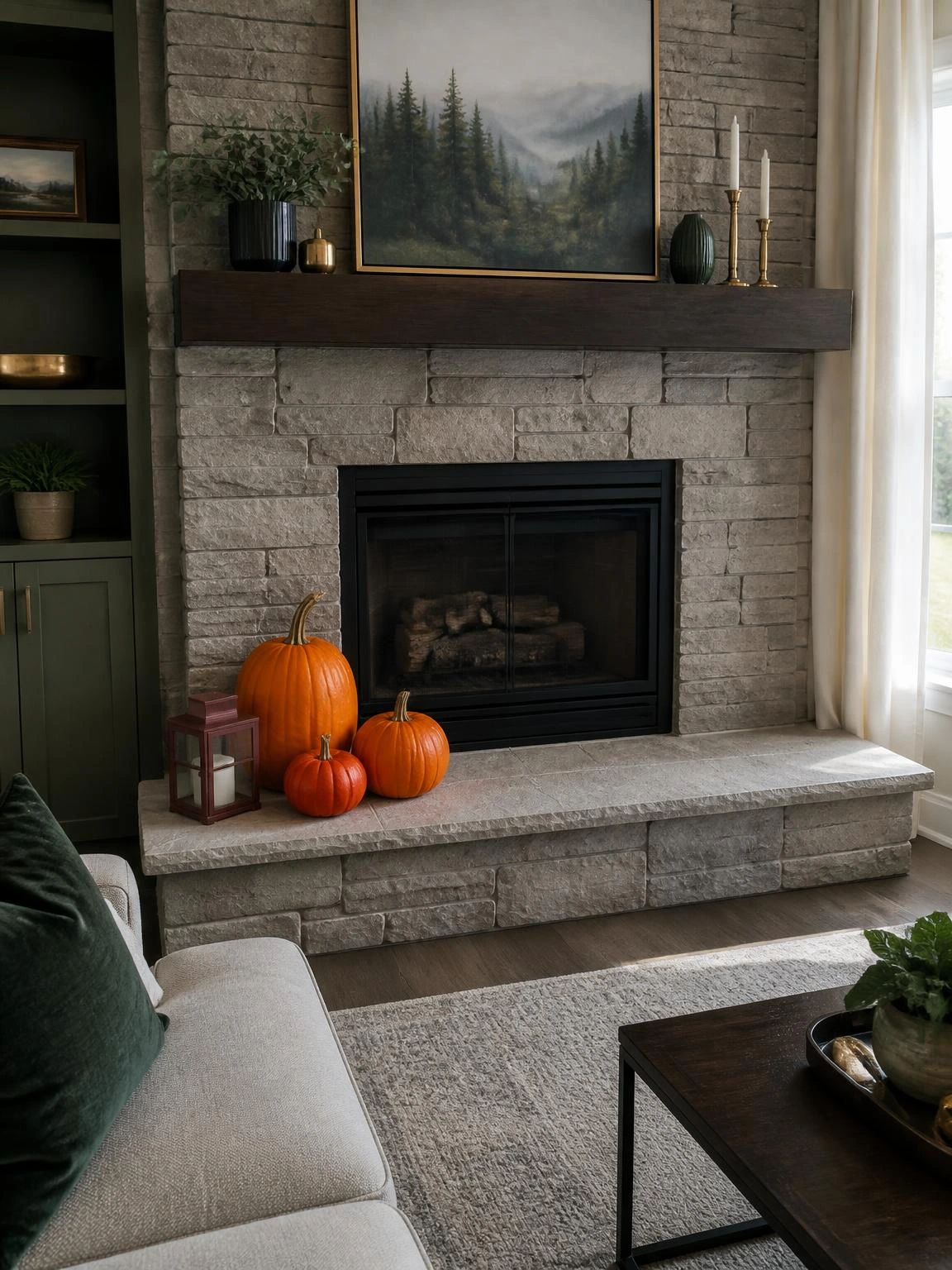 Halloween fireplace hearth decor with three orange pumpkins and a burgundy lantern arranged safely on a warm-gray stone hearth