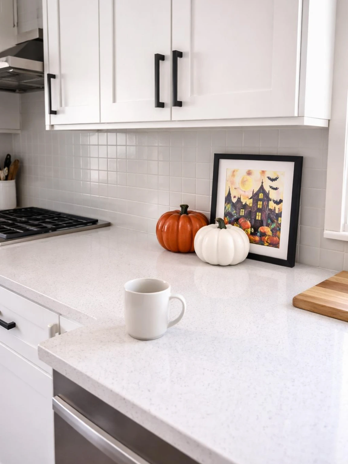 Halloween kitchen counter decor with two ceramic pumpkins and a seasonal print, leaving the quartz workspace open