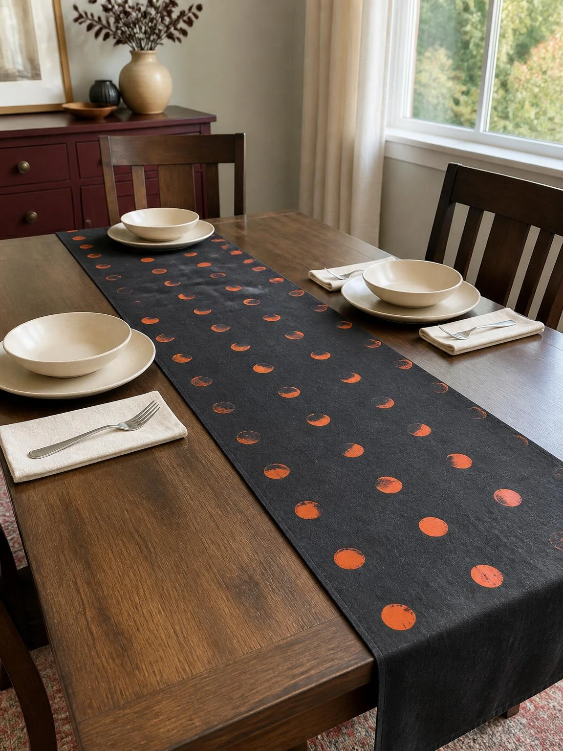 Charcoal cotton Halloween table runner with orange moon stamps centered on a dining table for an attainable DIY project