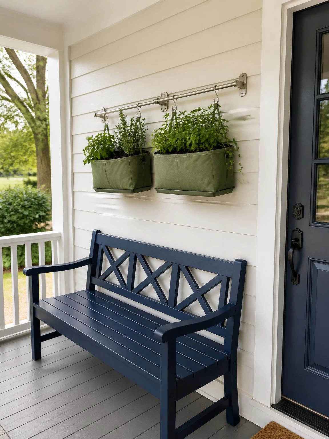 Brushed-metal hanging basket rail holds two herb-filled fabric baskets above a navy bench on an ivory porch wall for DIY garden projects