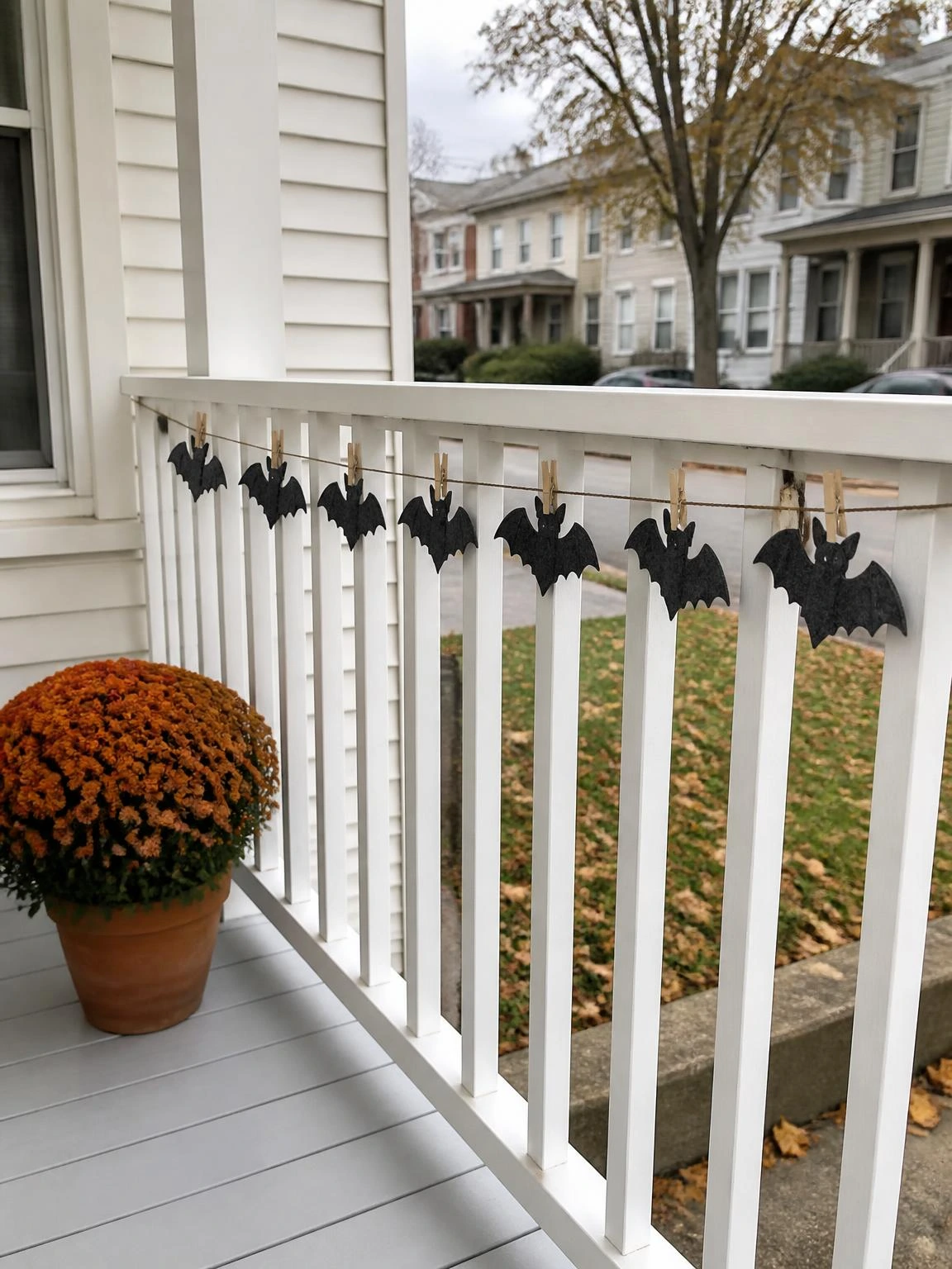 Charcoal gray felt bat garland clipped to a white porch railing with wooden clothespins, a simple Halloween porch idea for narrow row-house spaces
