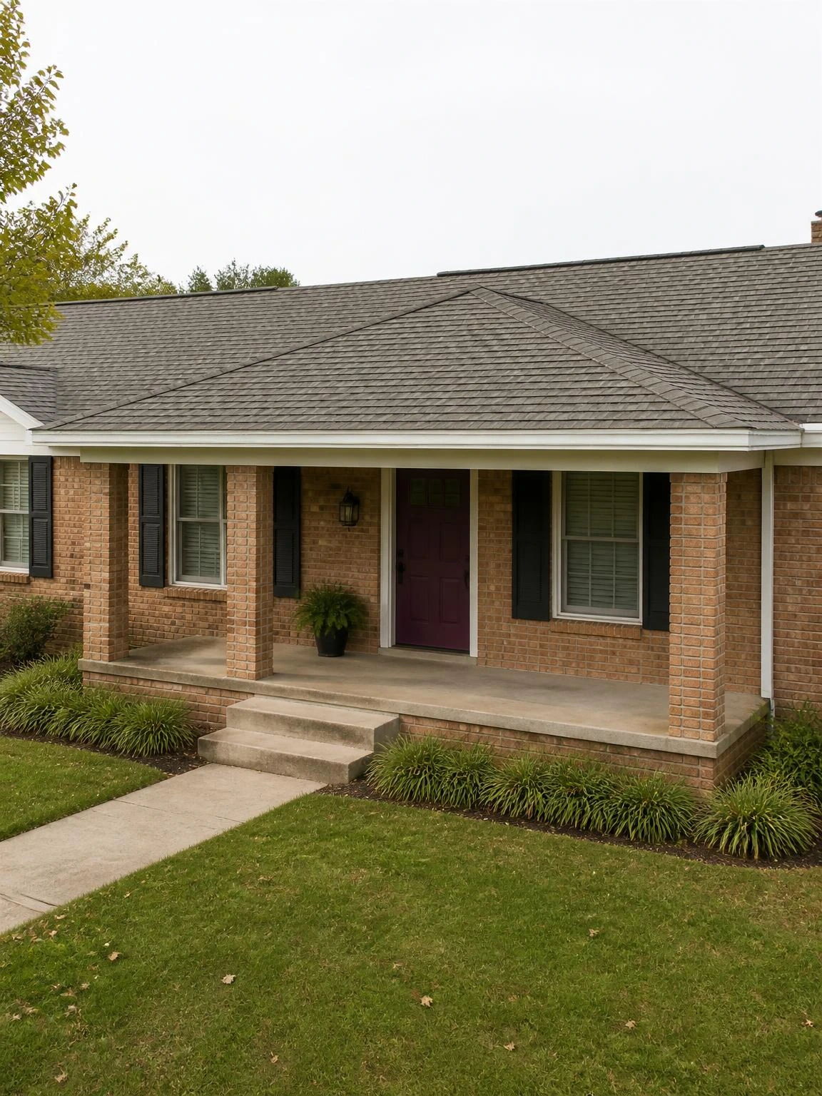 Hip roof porch addition spanning the full width of a brick ranch entry, with stone-gray shingles matched to the main roof and brick columns anchoring each corner