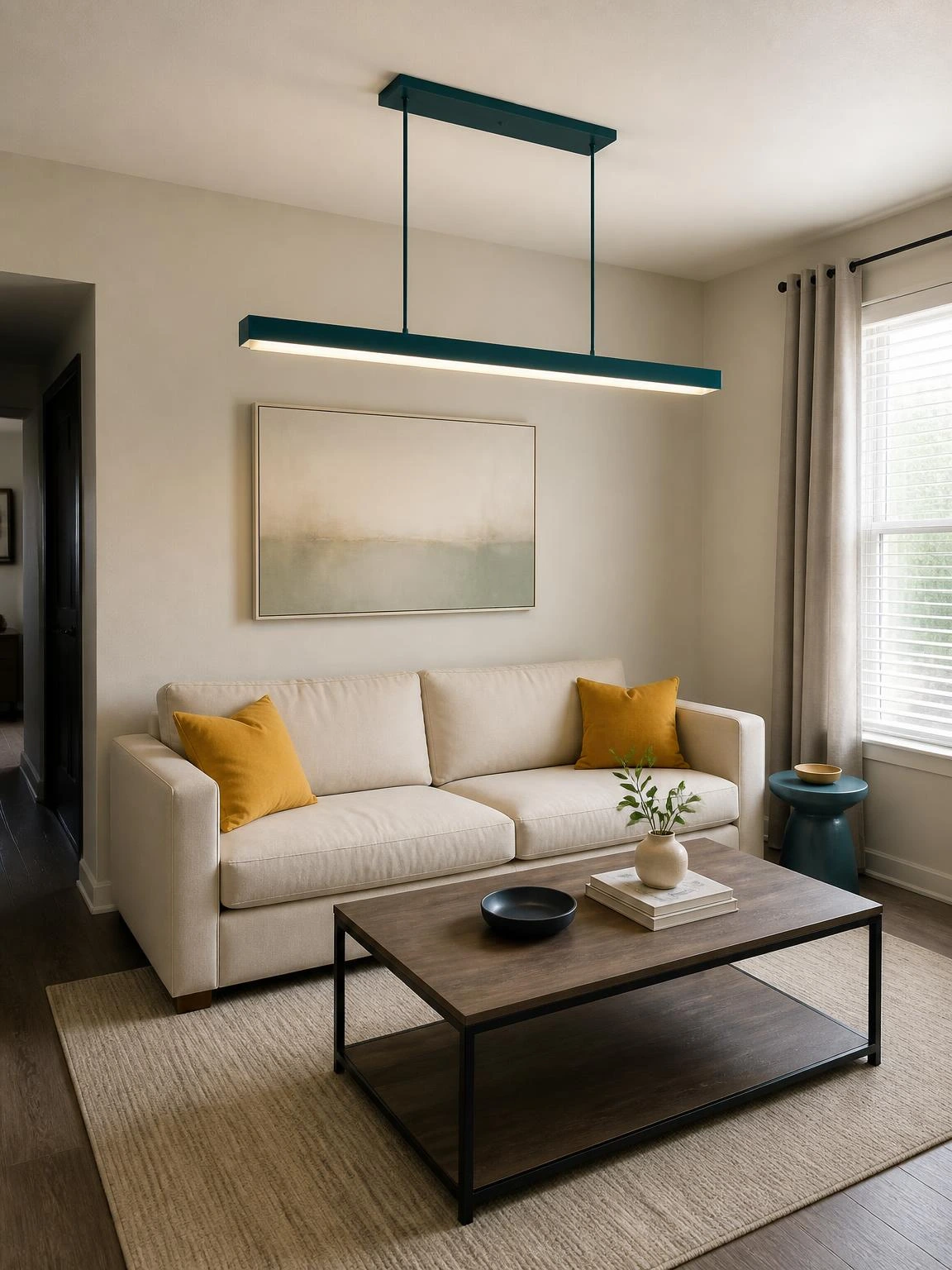 Deep-teal linear chandelier aligned over a sofa and coffee table, illustrating living room chandelier ideas for compact seating layouts