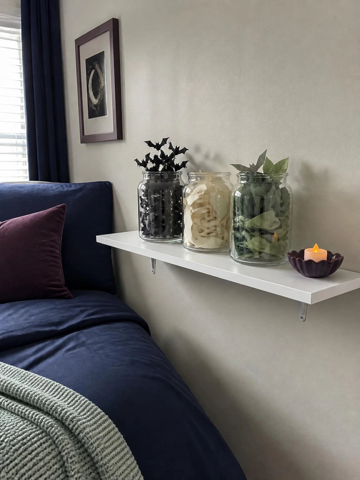 Budget Halloween shelf display with three glass containers of paper bats, moons, and leaves beside a navy bed