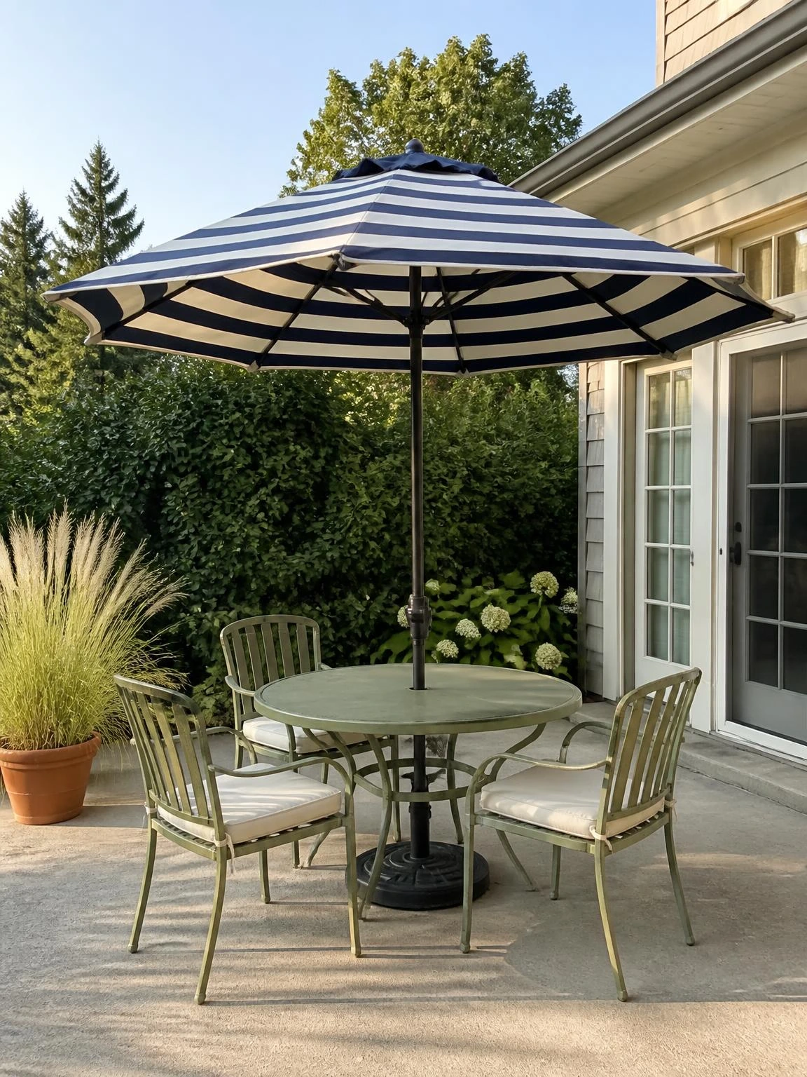 Navy and ivory striped market umbrella shading a round concrete patio table with sage-green chairs, a classic summer outdoor decor pairing