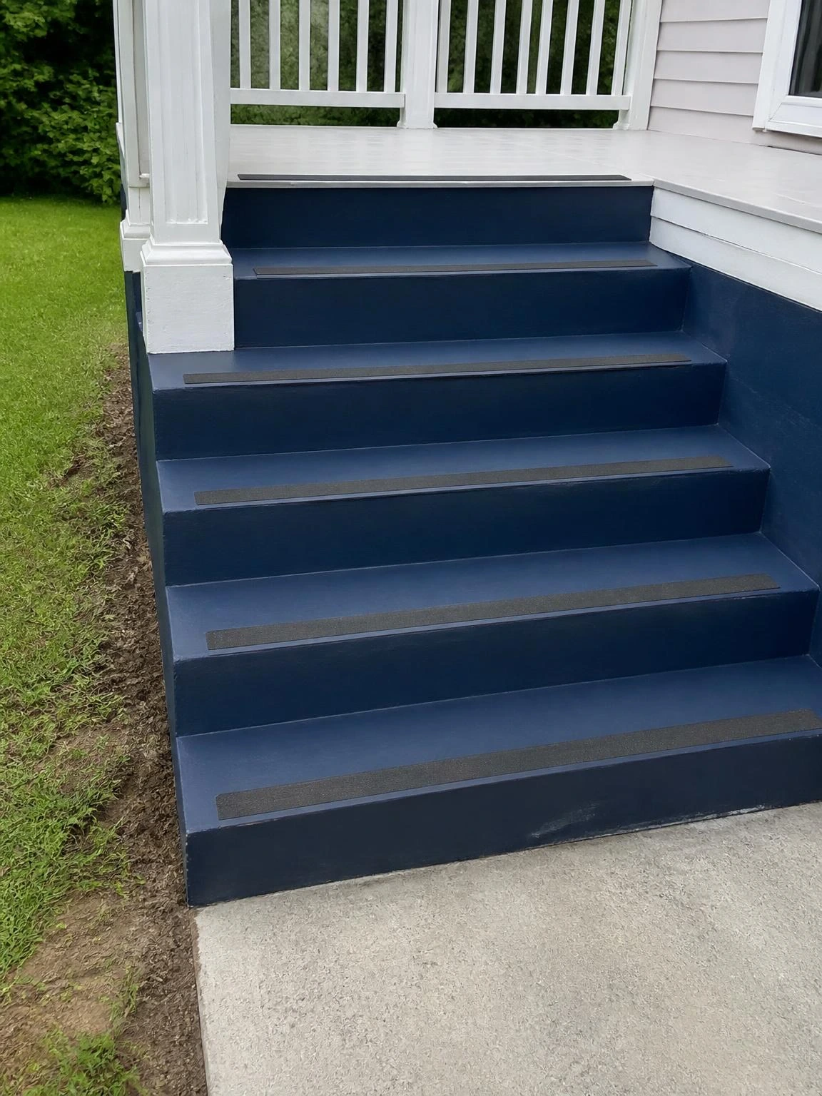 Deep navy painted concrete landscape stairs with charcoal anti-slip strips on each tread nosing, descending from a white deck to a gray path below