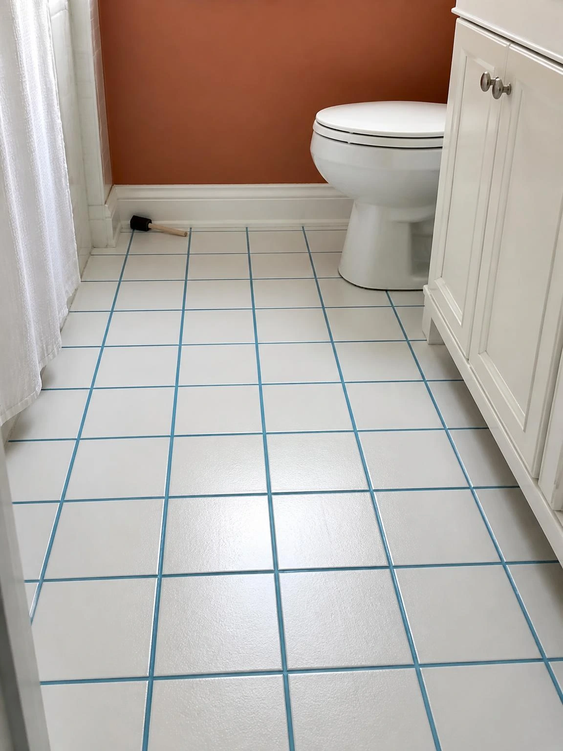 Compact bathroom floor with white ceramic tiles and freshly painted dusty-blue grout lines, a budget-friendly refresh that transforms the look of plain tile