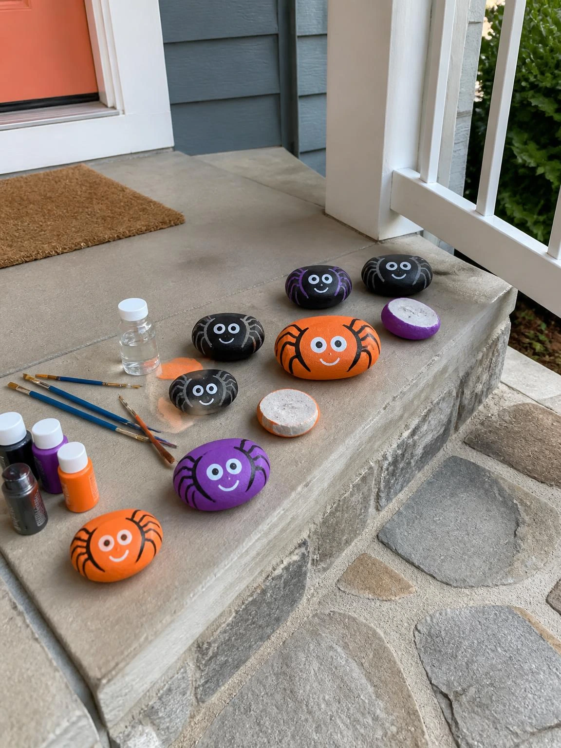 Painted rock spiders in black, plum, and orange cluster on a porch step, showcasing halloween crafts diy projects