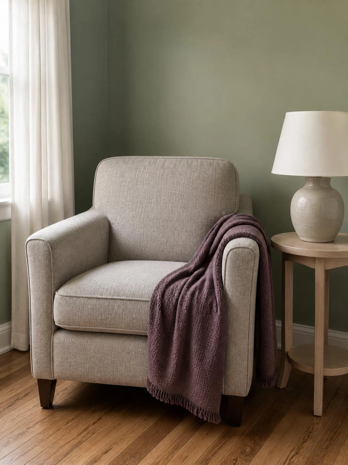 Muted plum cotton throw draped over a stone armchair arm against sage green wall — effortless summer living room color pairing