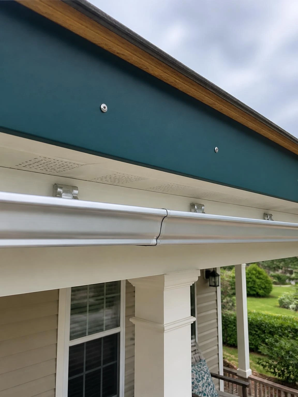 Deep teal cellular PVC fascia board with flush stainless screws installed on a residential porch roof eave, showing clean gutter attachment and proper fascia upgrade detail