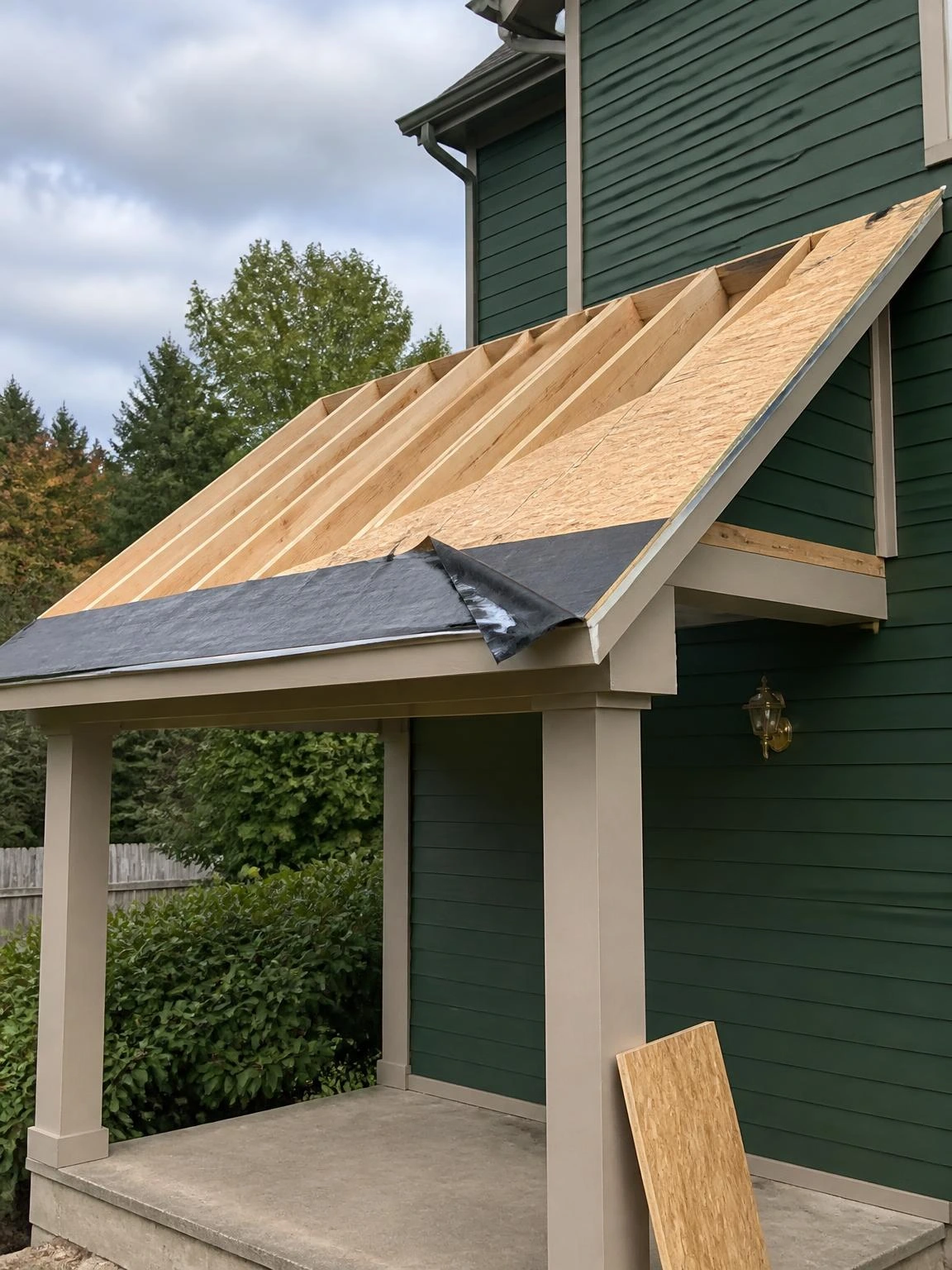 Re-framed porch roof mid-renovation showing new dimensional lumber rafters raising pitch to 4:12 for improved drainage, with partial OSB sheathing and ice membrane at eave