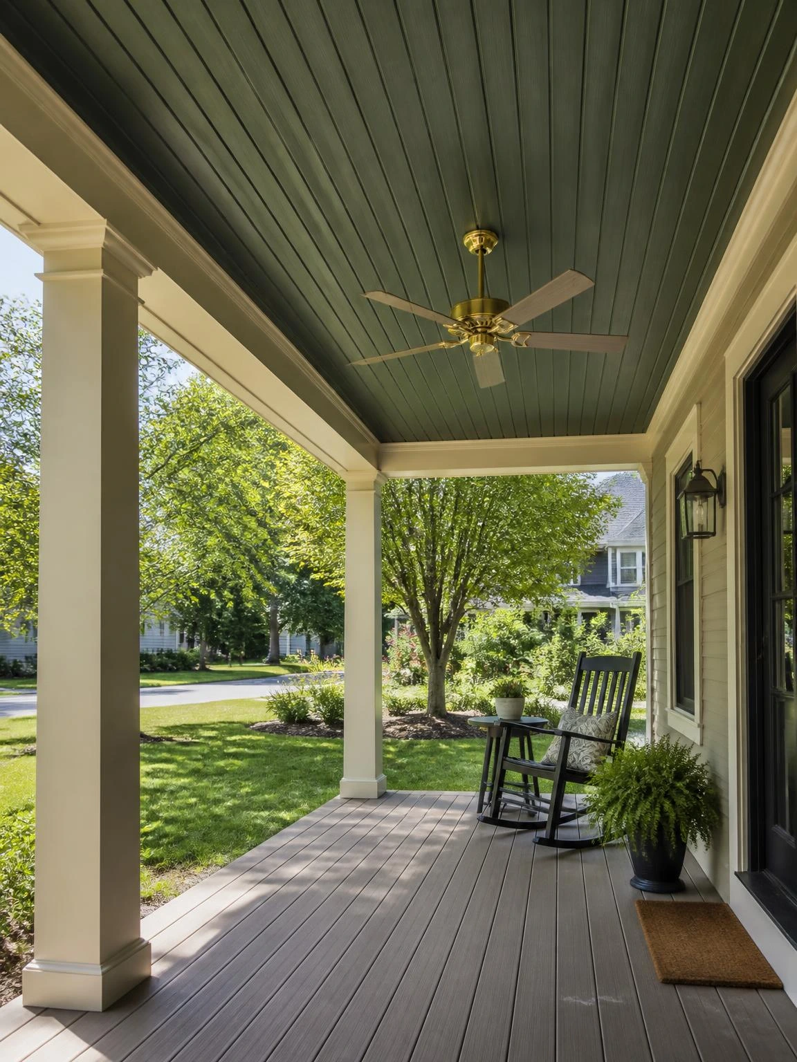 Forest green tongue-and-groove pine porch ceiling with brass ceiling fan mounted to structural joist, framed by cream columns and composite decking