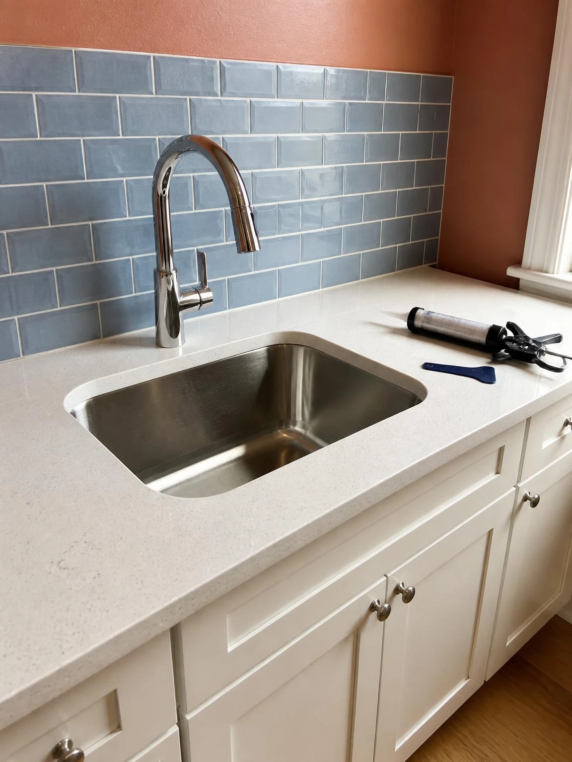 Fresh clear silicone caulk sealing a stainless undermount sink to white quartz countertop, a key DIY kitchen sink re-caulk result
