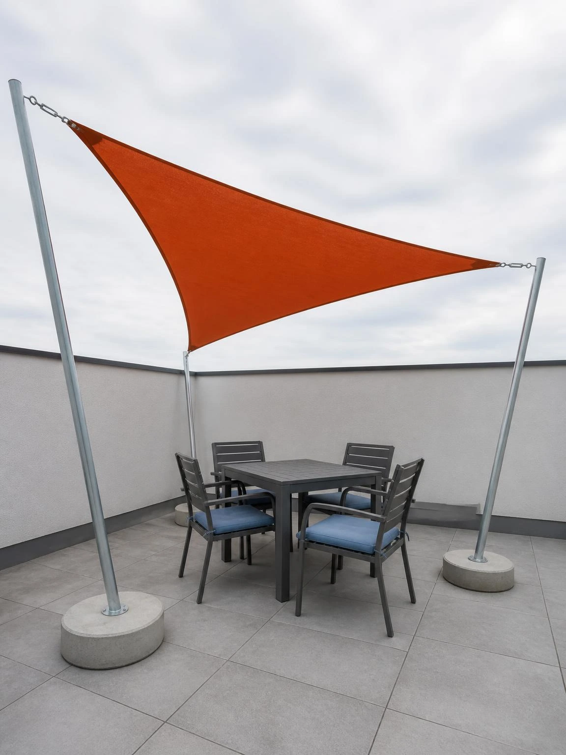 Rust-orange triangular shade sail tensioned between three galvanised poles above a compact rooftop terrace dining set for small rooftop terrace design