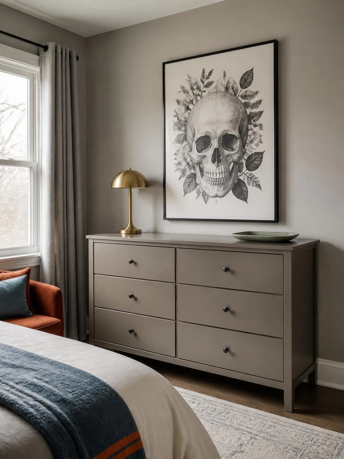 Monochrome skull wall art anchors a warm gray bedroom dresser, showing attainable Halloween aesthetic bedroom decor with brass and green accents.