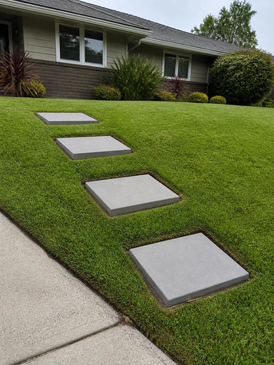 Four 24-inch square concrete stepping stones ascend a gentle front yard grass slope, showing how landscape stairs work on low residential grades