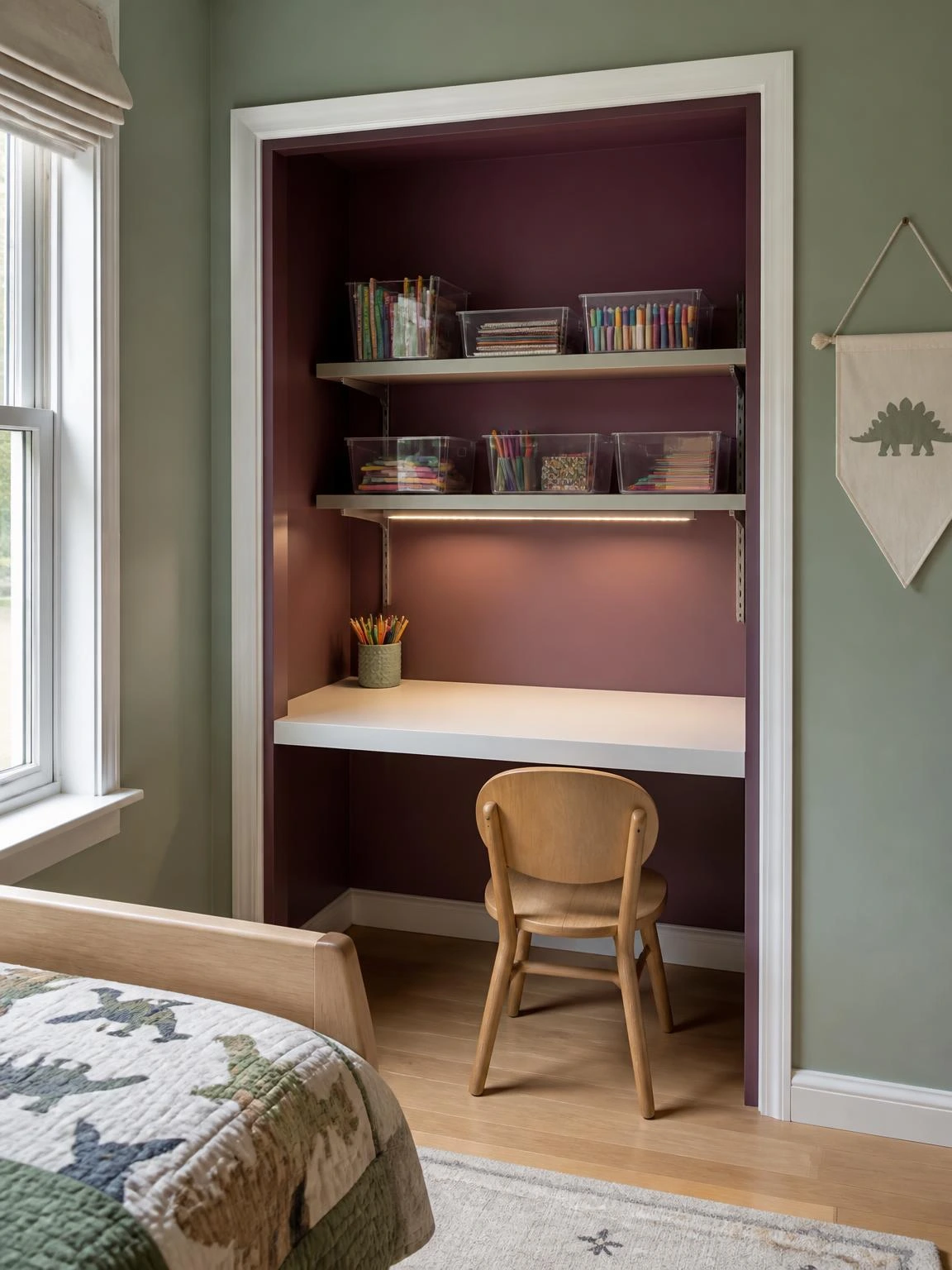 Kids' study table built into a closet nook with plum interior walls, white laminate desk, and organized acrylic shelf bins in a sage green bedroom