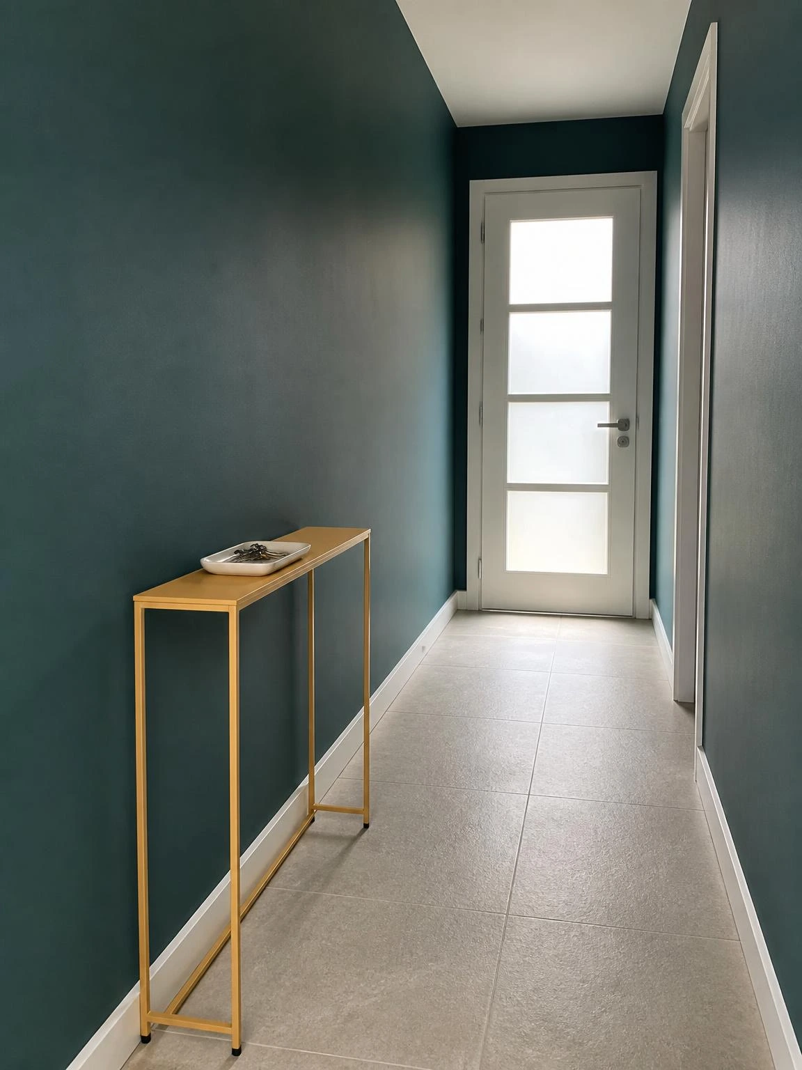 Narrow hallway with deep teal walls and a slim mustard console table holding a ceramic tray — a minimal home decor idea for tight spaces